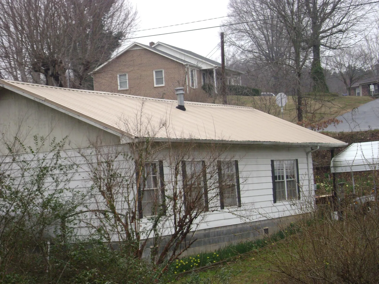 Tan metal roof on a white sided house set into a hillside — Commercial Roofing by Roofing Brothers in Sumner